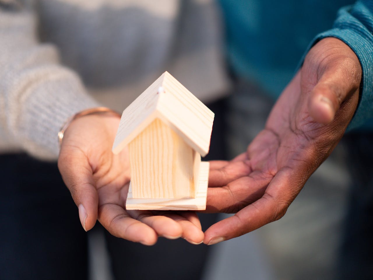 services-02 Hands holding a small wooden house model, symbolizing new home ownership and real estate transactions.